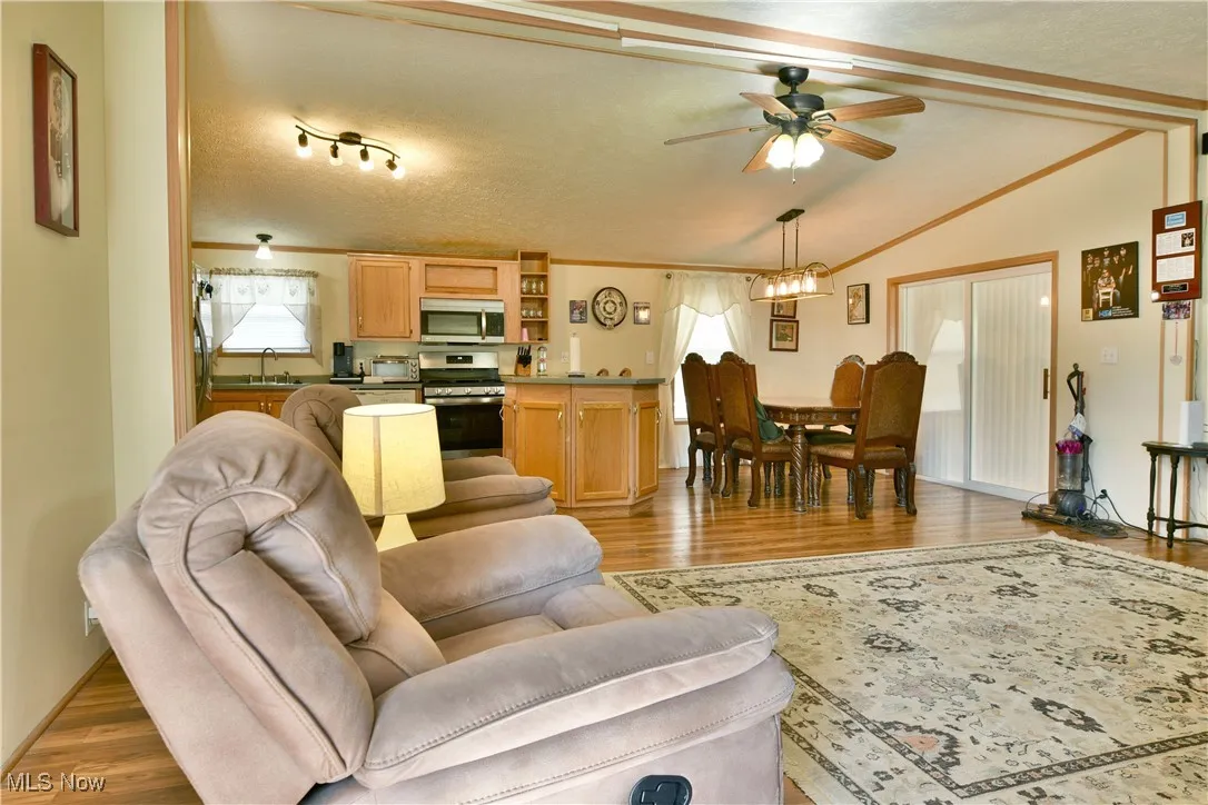 Living area with light wood finished floors, crown molding, a ceiling fan, vaulted ceiling, and a textured ceiling