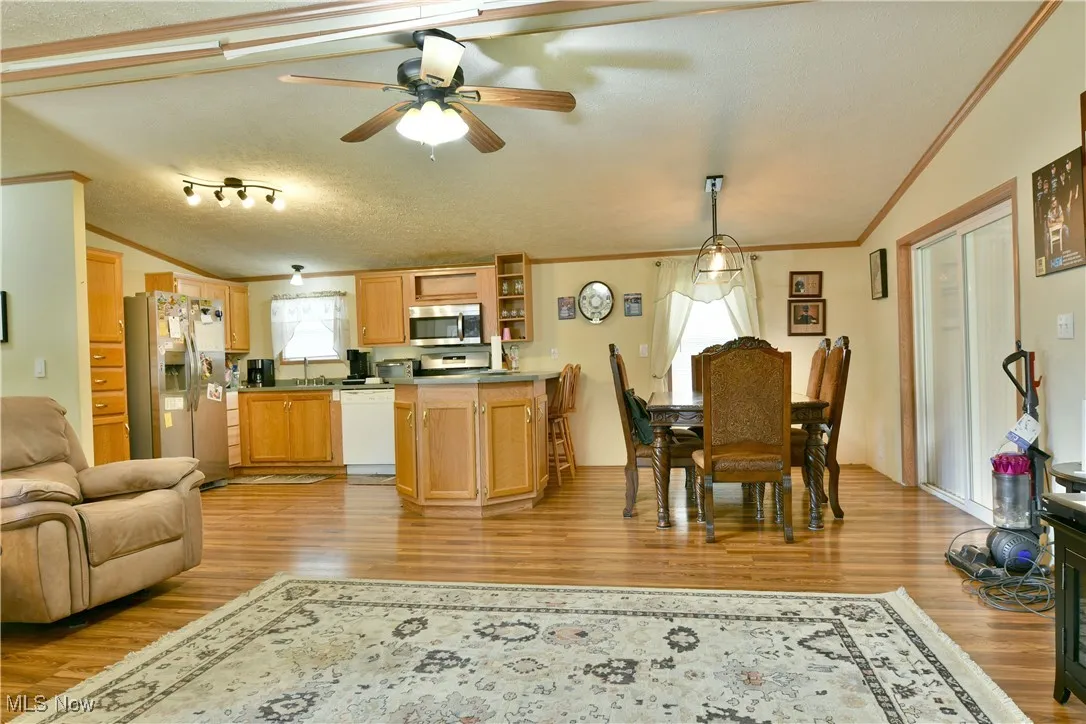Dining space featuring ornamental molding, ceiling fan, light wood-style floors, vaulted ceiling, and a textured ceiling