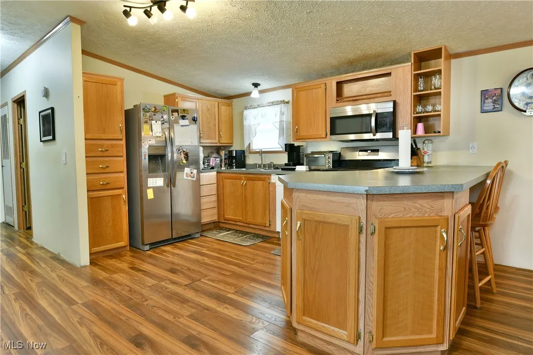Kitchen featuring a peninsula, appliances with stainless steel finishes, open shelves, a textured ceiling, and crown molding