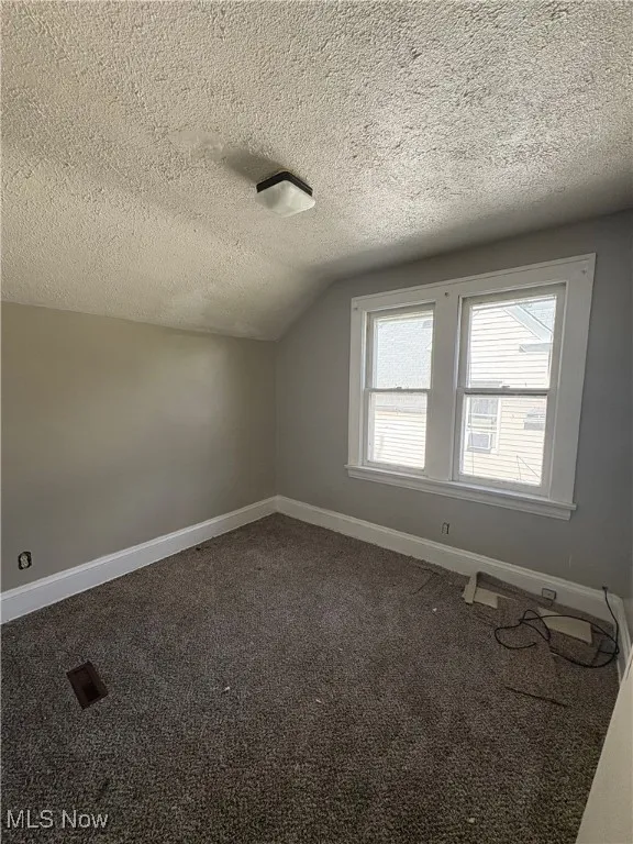 Bonus room with dark colored carpet, a textured ceiling, and lofted ceiling