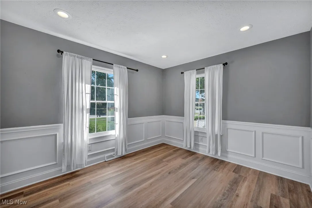 Empty room with healthy amount of natural light, a decorative wall, a wainscoted wall, light wood-style floors, and a textured ceiling