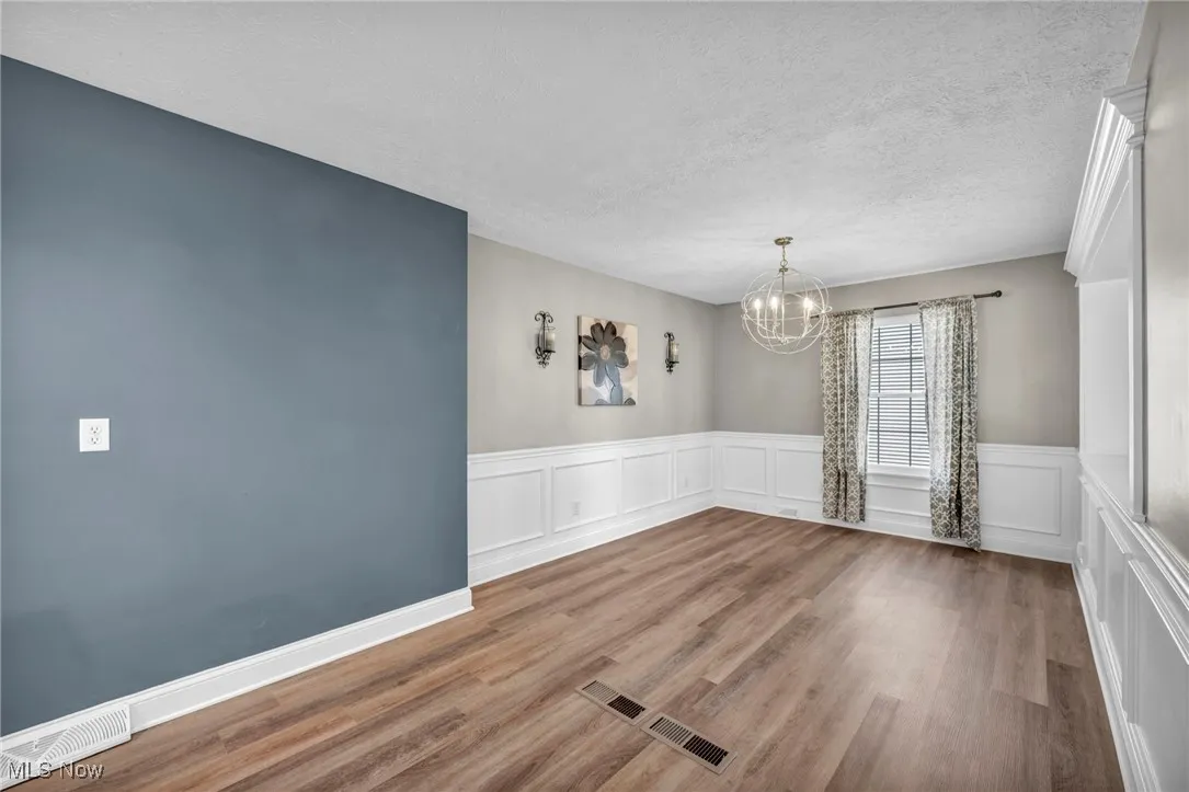 Unfurnished dining area with light wood-style flooring, a textured ceiling, a chandelier, a wainscoted wall, and a decorative wall