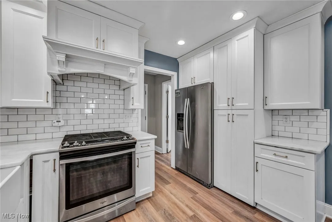 Kitchen with appliances with stainless steel finishes, decorative backsplash, white cabinetry, light wood-type flooring, and recessed lighting