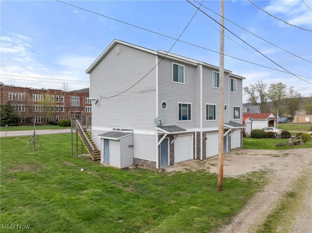 Back of house featuring driveway, a lawn, stairway, and a garage