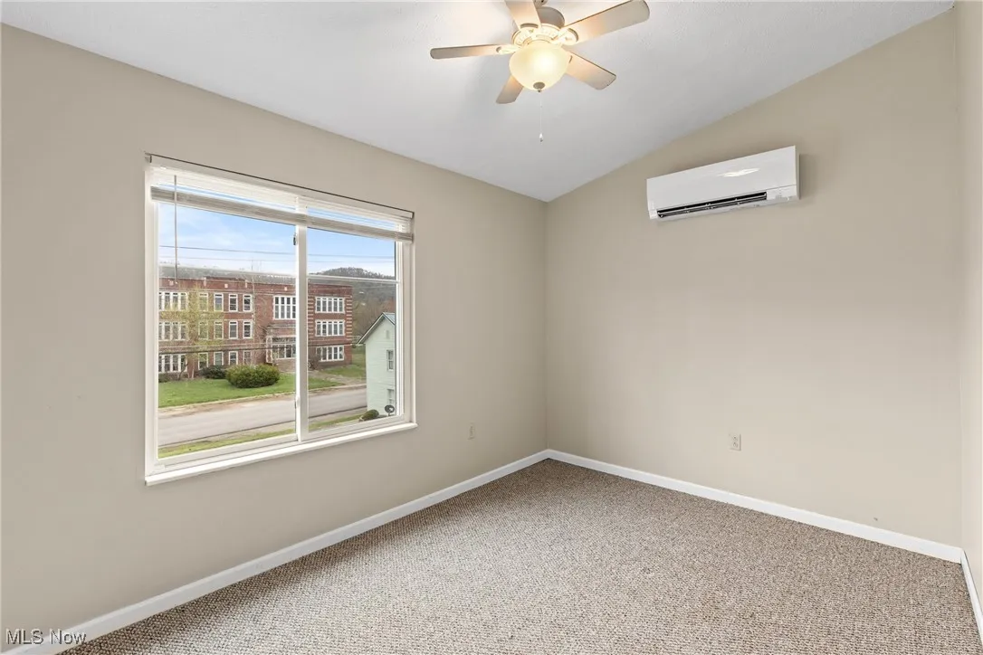 Carpeted empty room with lofted ceiling, a wall mounted air conditioner, and a ceiling fan