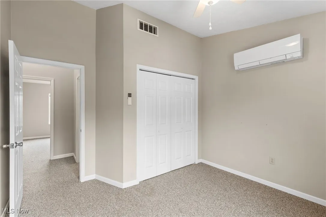 Unfurnished bedroom featuring carpet floors, an AC wall unit, a closet, and a ceiling fan