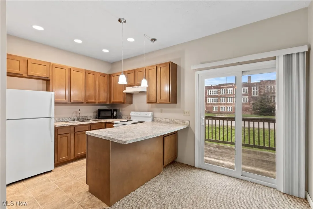 Kitchen with white appliances, light countertops, decorative light fixtures, a peninsula, and brown cabinets