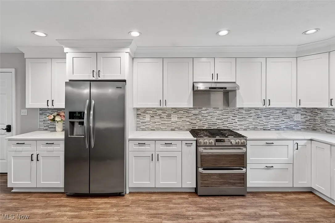 Kitchen with appliances with stainless steel finishes, white cabinets, recessed lighting, tasteful backsplash, and light wood-style floors
