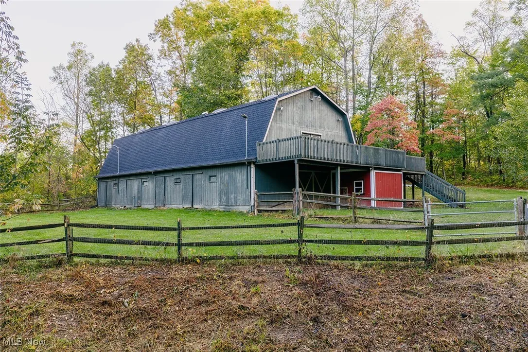 Barn featuring a gambrel roof, a barn, an outdoor structure, view of wooded area, and a wooden deck