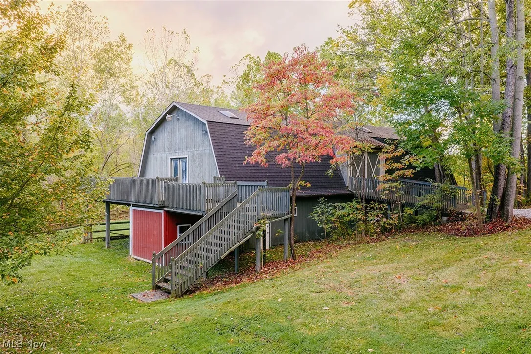 Rear view of out building featuring a gambrel roof, stairway, a lawn, and a wooden deck