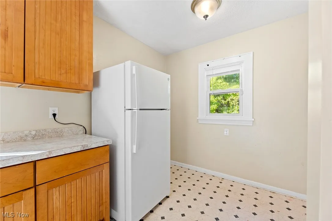 Kitchen with freestanding refrigerator, light countertops, brown cabinetry, and light floors