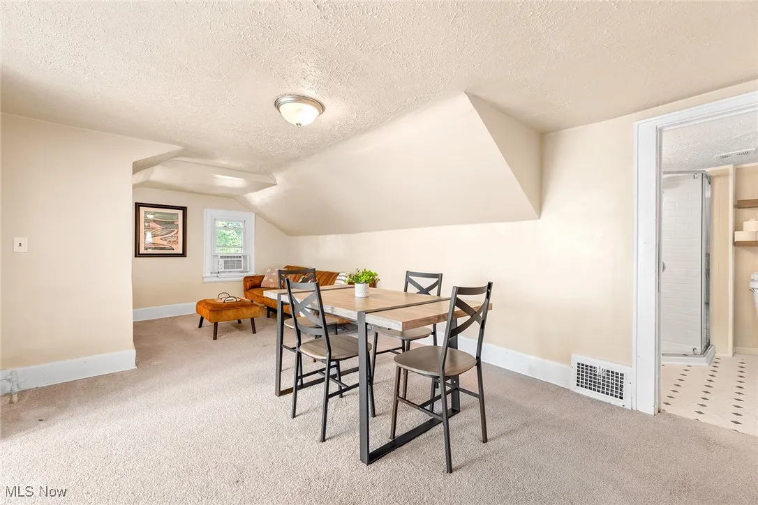 Dining space with a textured ceiling, light carpet, and vaulted ceiling