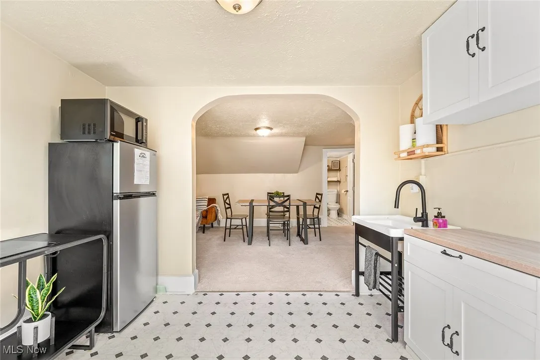 Kitchen featuring a textured ceiling, arched walkways, white cabinets, freestanding refrigerator, and light floors