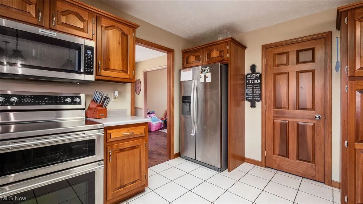 Kitchen featuring stainless steel appliances, brown cabinets, light countertops, and light tile patterned floors