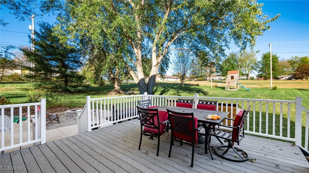 Wooden terrace featuring a playground, outdoor dining area, and a yard