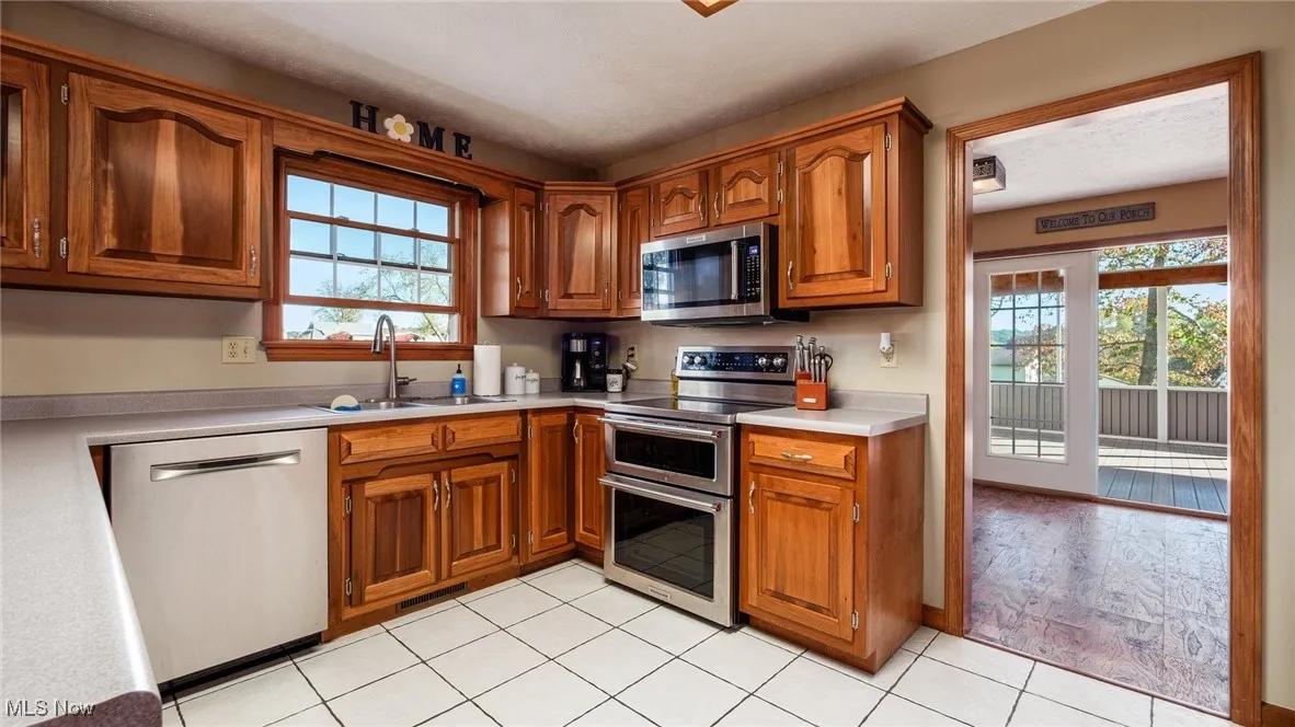 Kitchen with stainless steel appliances, light countertops, brown cabinets, and light tile patterned floors
