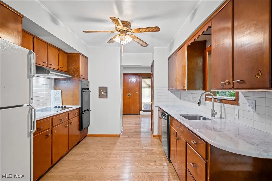 Kitchen featuring backsplash, brown cabinets, black appliances, light wood finished floors, and crown molding