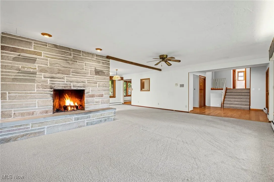 Unfurnished living room featuring carpet floors, stairway, a fireplace, ceiling fan, and baseboard heating