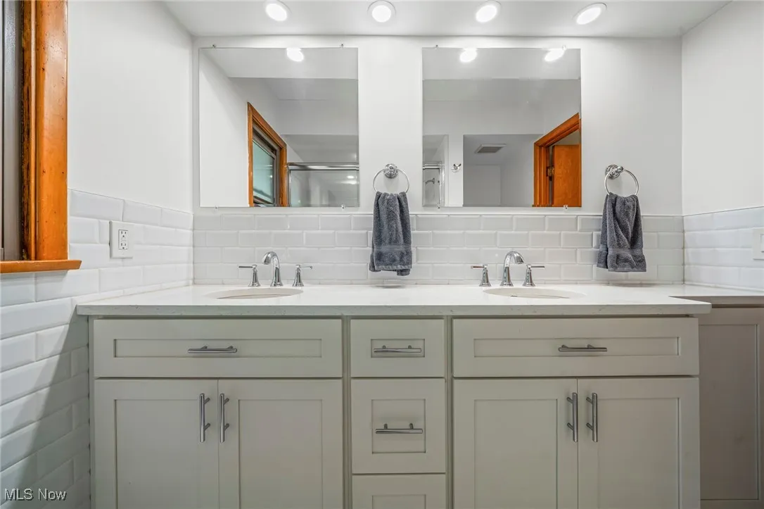 Bathroom with a shower with door, double vanity, and decorative backsplash