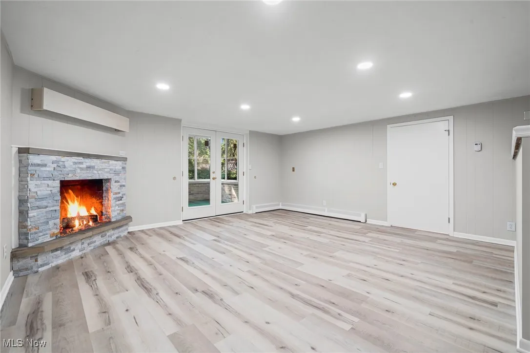 Unfurnished living room with wooden walls, light wood-type flooring, a fireplace, french doors, and recessed lighting