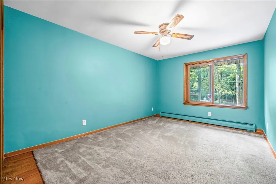 Unfurnished room featuring a baseboard heating unit, a ceiling fan, and carpet floors