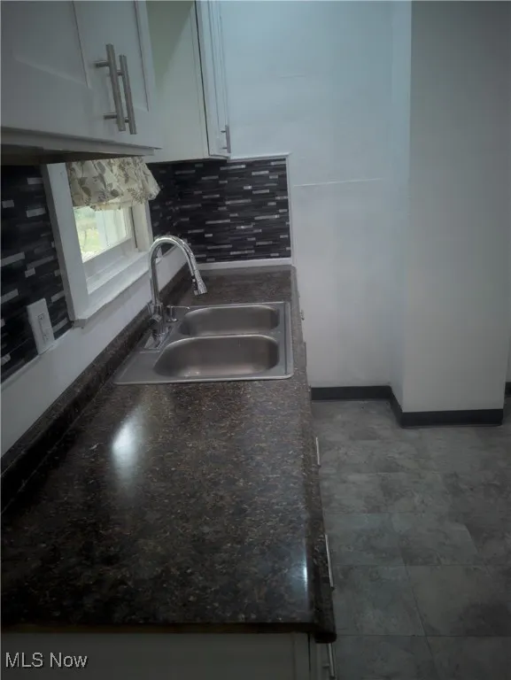 Kitchen with dark countertops, white cabinets, and backsplash