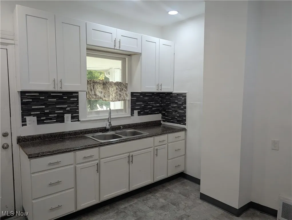 Kitchen with dark countertops, tasteful backsplash, and white cabinets