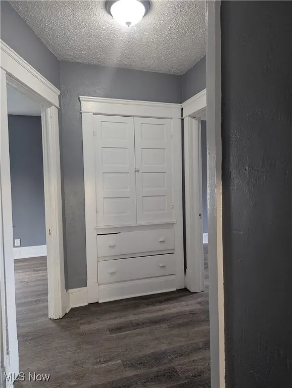 Hallway featuring a textured wall, dark wood-type flooring, and a textured ceiling