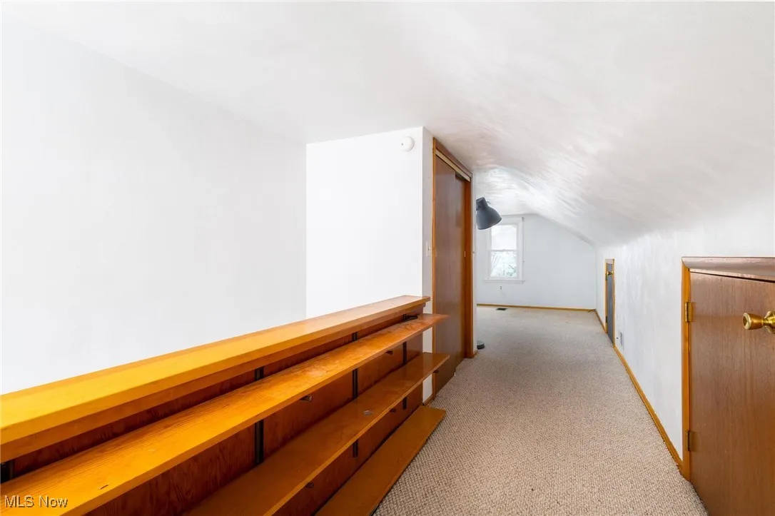 Corridor featuring light colored carpet and vaulted ceiling