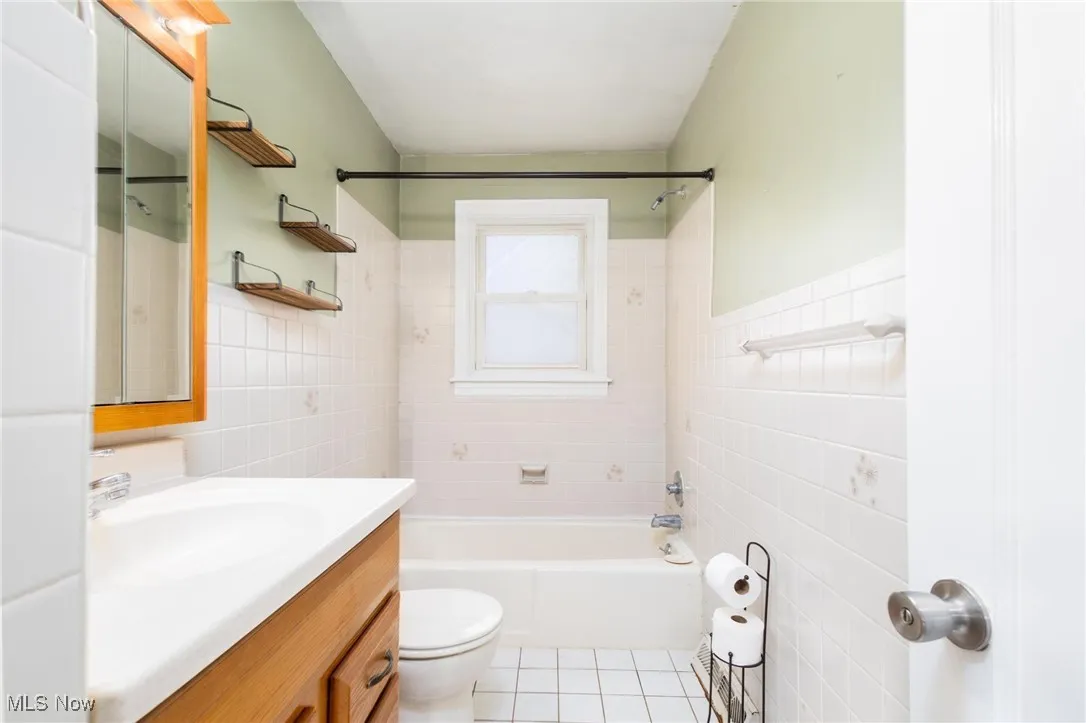 Full bath with tile walls, vanity, shower / bath combination, light tile patterned floors, and wainscoting
