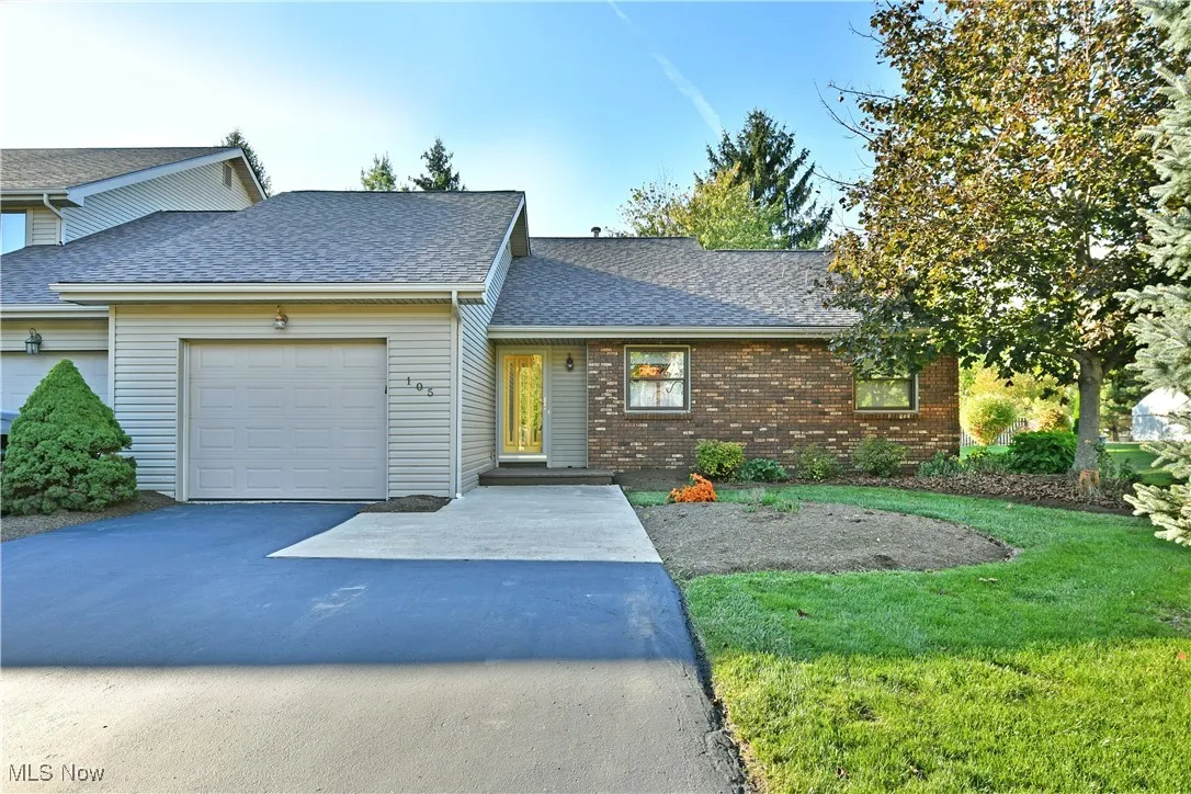 View of front of property with a shingled roof, driveway, brick siding, an attached garage, and a front yard
