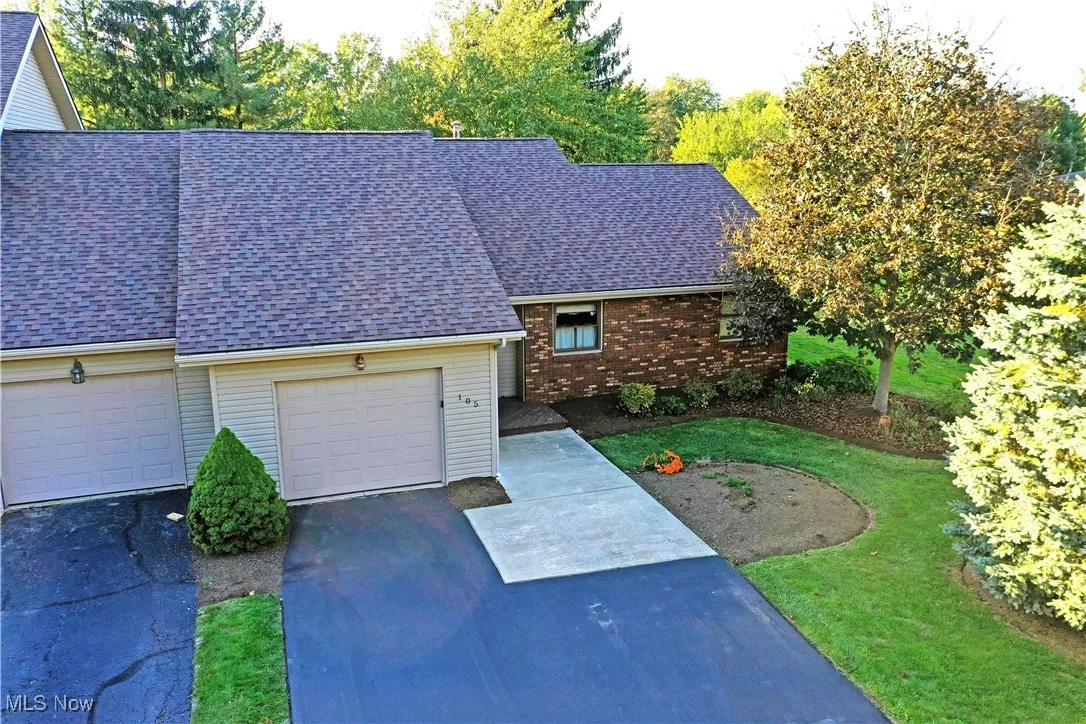 View of front of property featuring driveway, a garage, a shingled roof, a front yard, and brick siding
