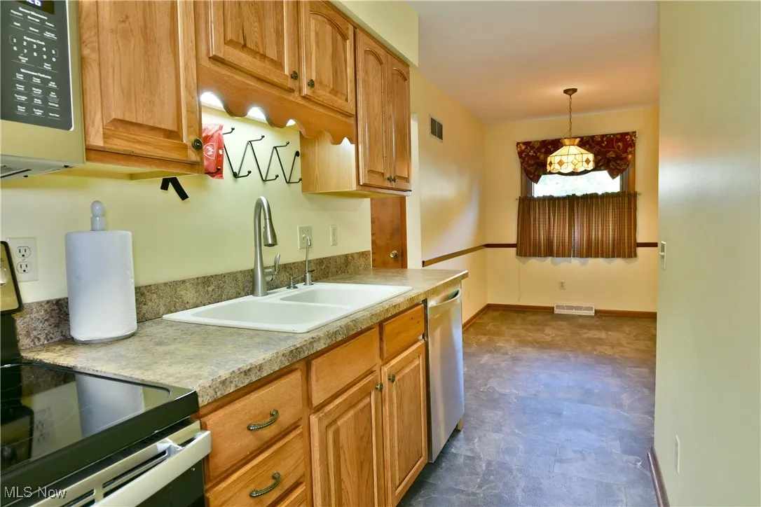 Kitchen with stainless steel appliances, pendant lighting, light countertops, and brown cabinetry