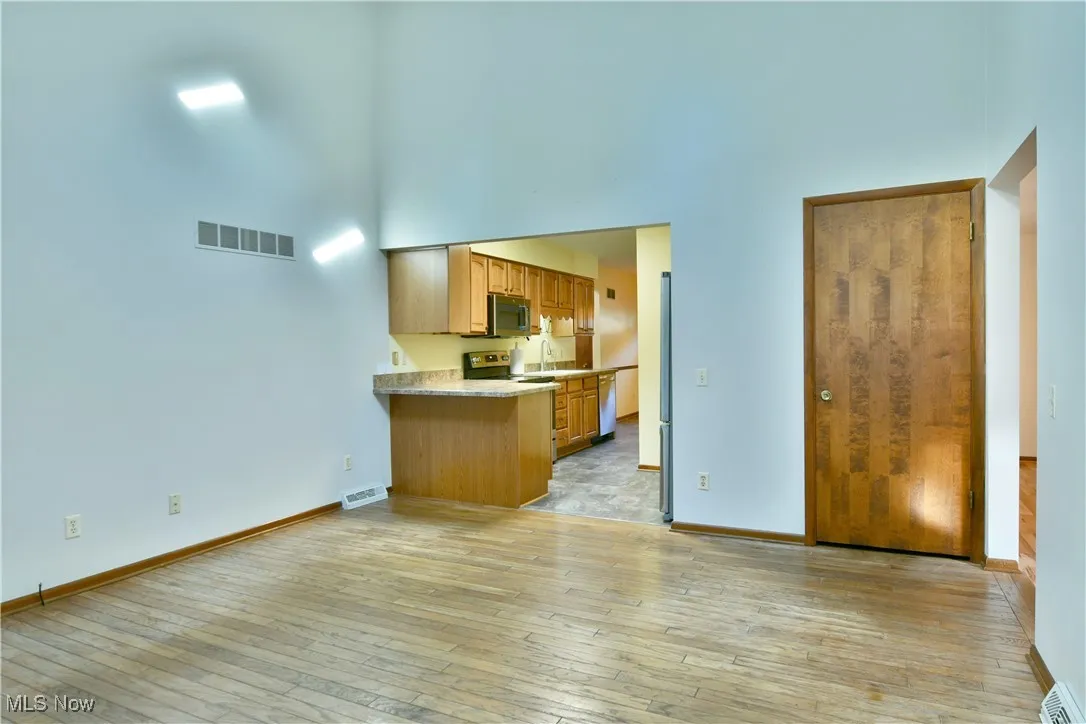 Kitchen featuring a towering ceiling, light wood-style flooring, a peninsula, and appliances with stainless steel finishes