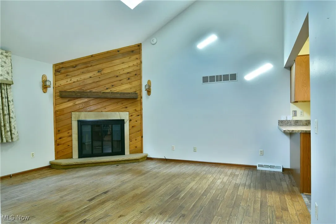 Unfurnished living room featuring light wood finished floors, a glass covered fireplace, and a towering ceiling