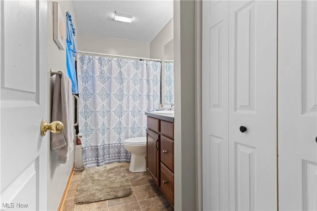 Bathroom with a closet, vanity, a shower with shower curtain, and a textured ceiling
