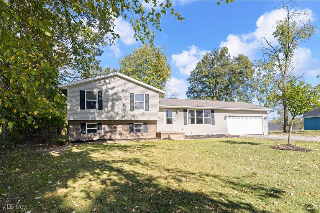 Tri-level home with brick siding, a front yard, an attached garage, and driveway