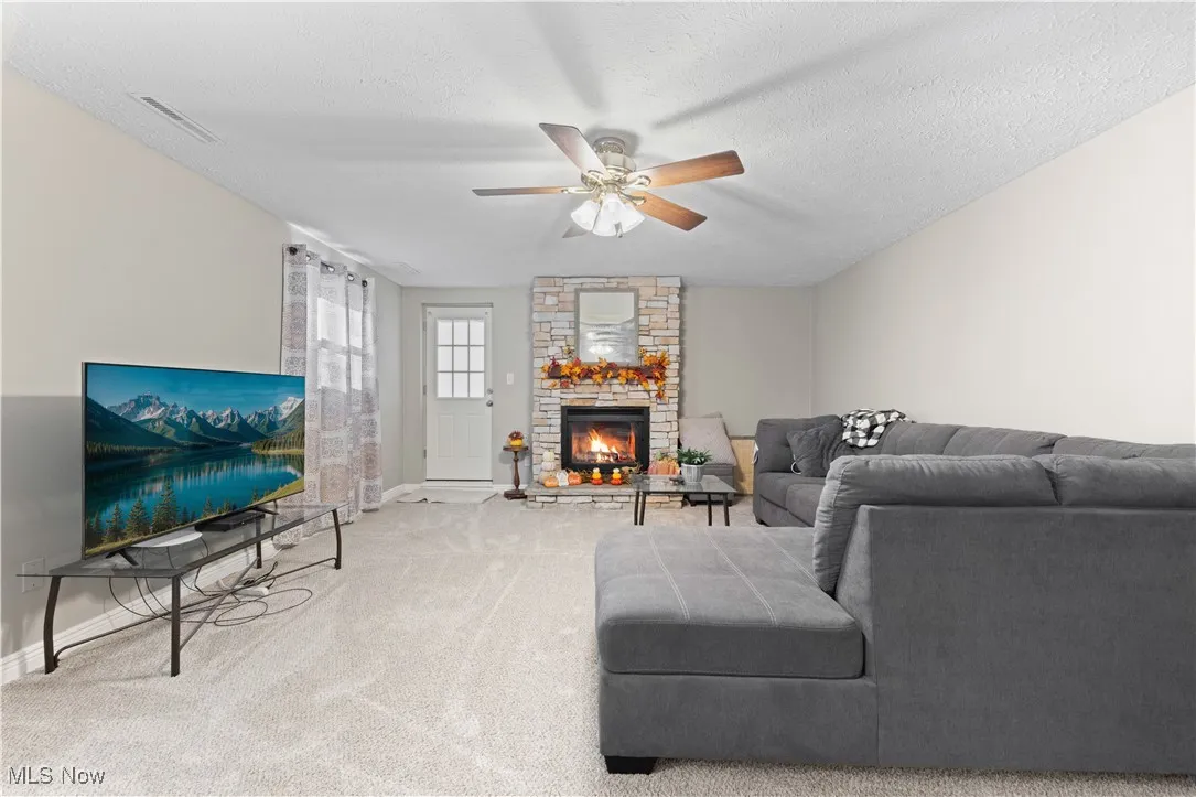 Living area featuring carpet, a ceiling fan, a textured ceiling, and a stone fireplace