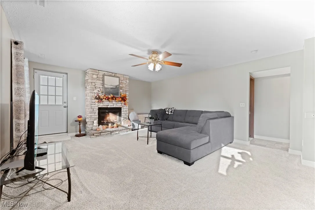 Living area featuring carpet, a ceiling fan, and a stone fireplace