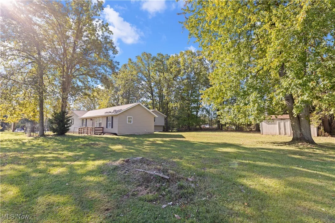 View of green lawn with a storage shed and view of wooded area