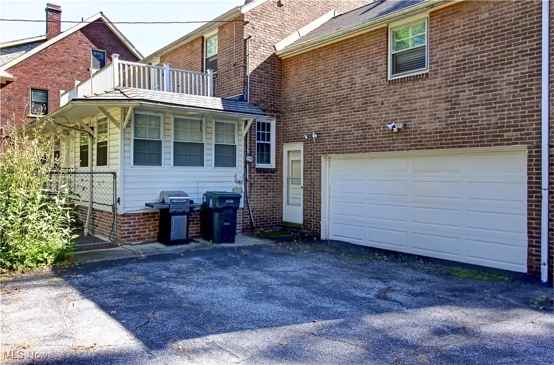 Back of property featuring an attached garage, asphalt driveway, a balcony, and brick siding