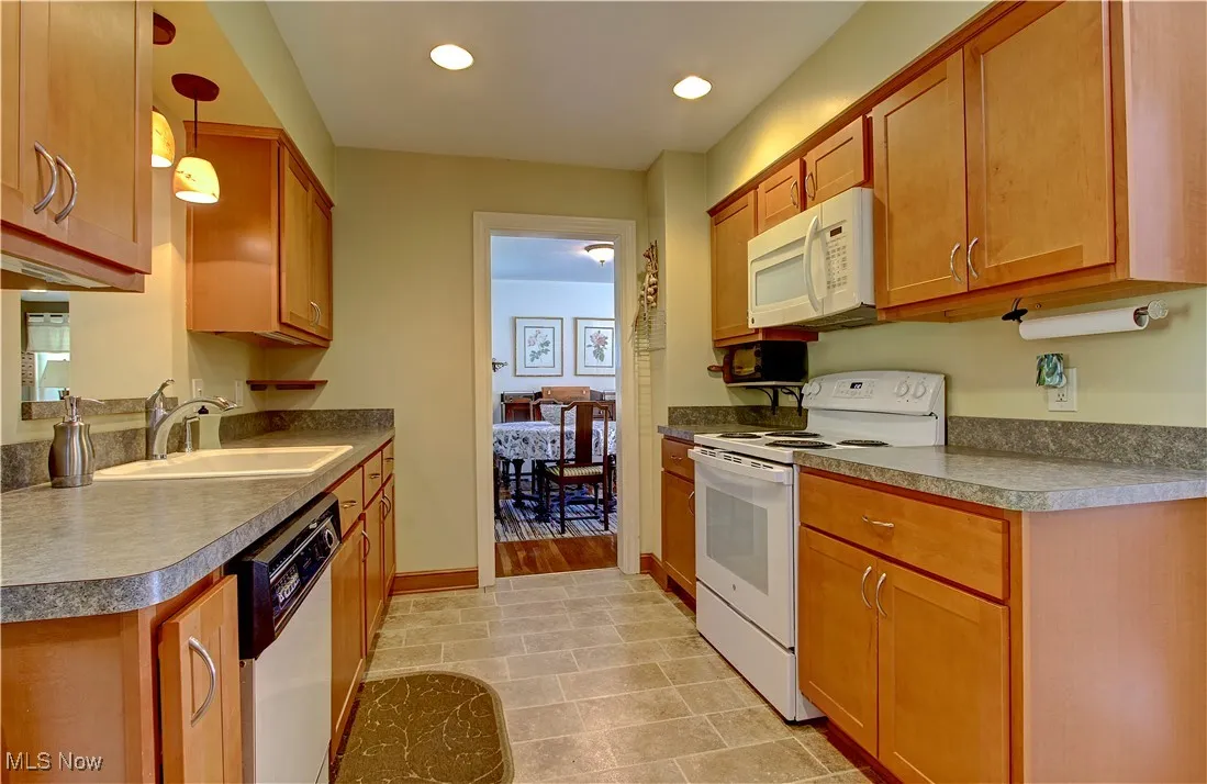 Kitchen with white appliances, decorative light fixtures, brown cabinetry, recessed lighting, and dark countertops