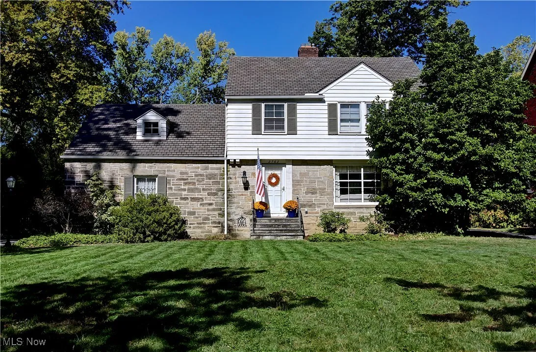View of front facade with stone siding, a front yard, and a chimney