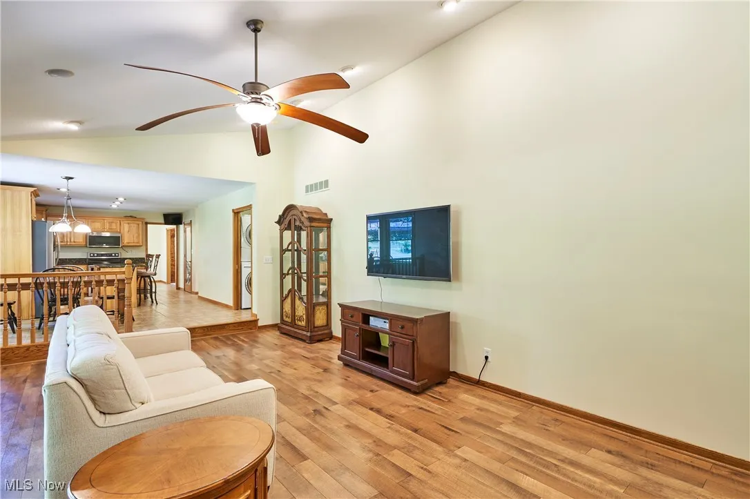 Living area featuring stacked washing machine and dryer, light wood finished floors, a ceiling fan, and high vaulted ceiling