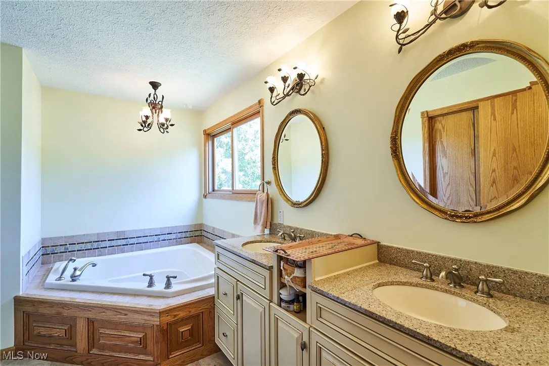 Full bathroom with vanity, a textured ceiling, a garden tub, and a chandelier