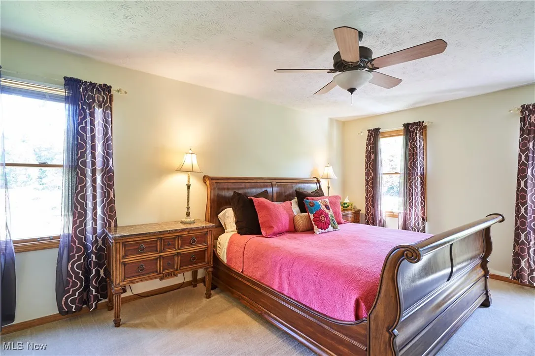 Bedroom with light colored carpet, a textured ceiling, multiple windows, and ceiling fan