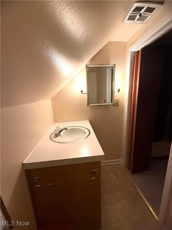 Bathroom featuring a textured ceiling, vanity, vaulted ceiling, and dark tile patterned flooring