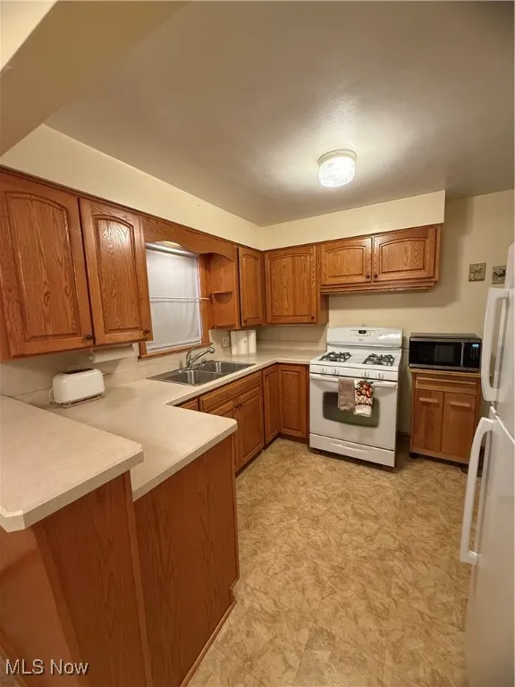 Kitchen with brown cabinetry, stove, fridge, light countertops, and a peninsula