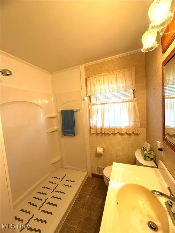 Full bath with plenty of natural light, a shower stall, dark tile patterned flooring, and ornamental molding
