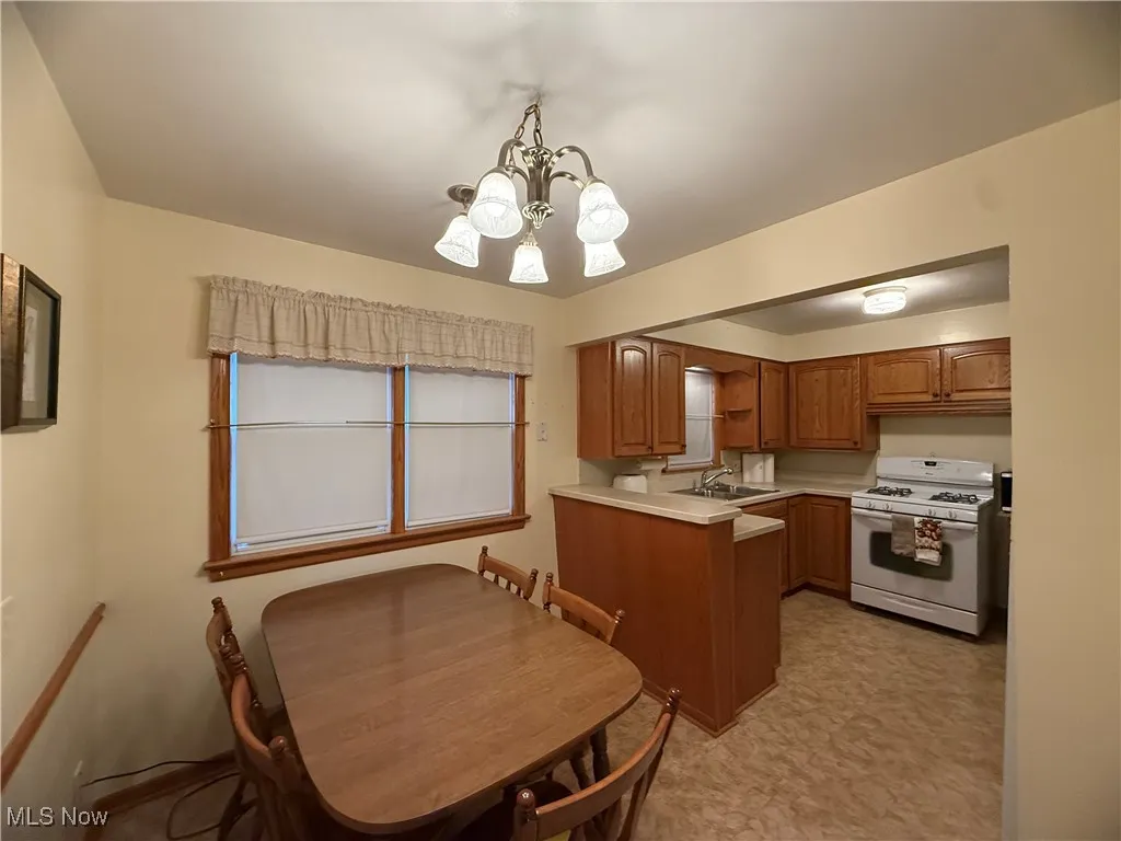 Kitchen with brown cabinetry, light countertops, white range with gas stovetop, pendant lighting, and a chandelier